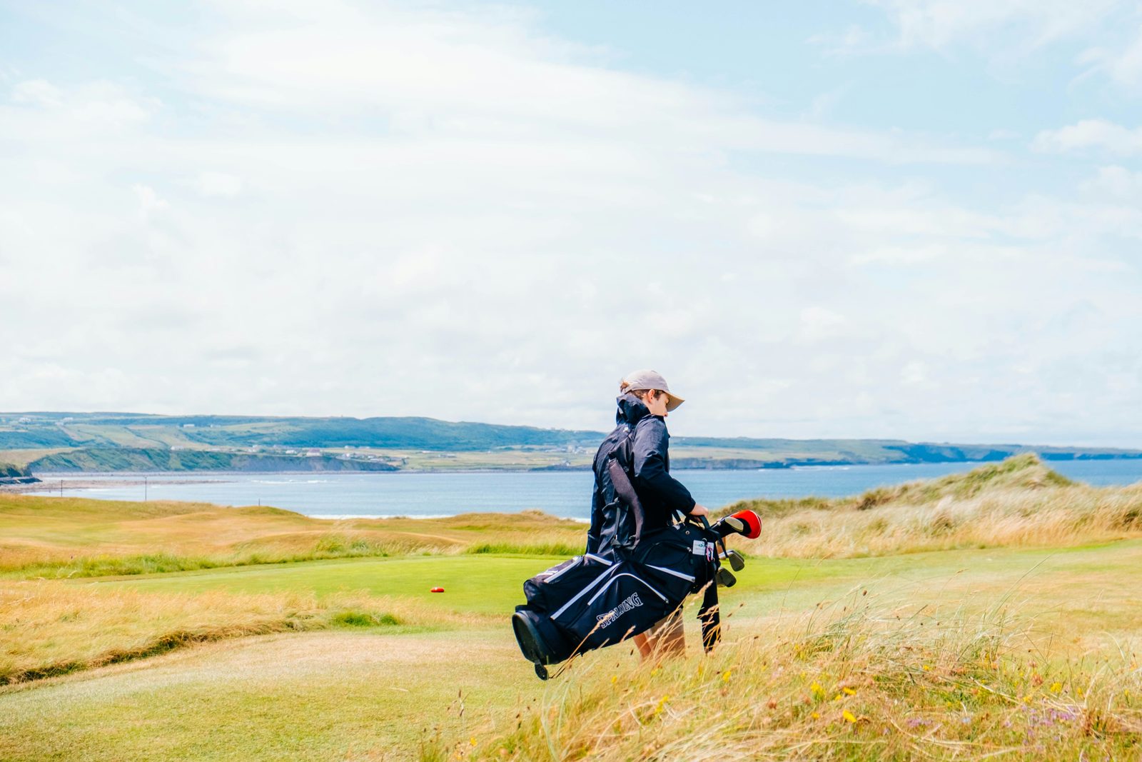 A golfer carrying his bag across links land beside the sea in Ireland